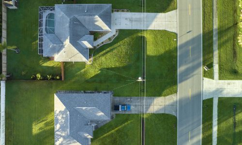 Aerial view of street traffic with driving cars in small town. American suburban landscape with private homes between green palm trees in Florida quiet residential area.