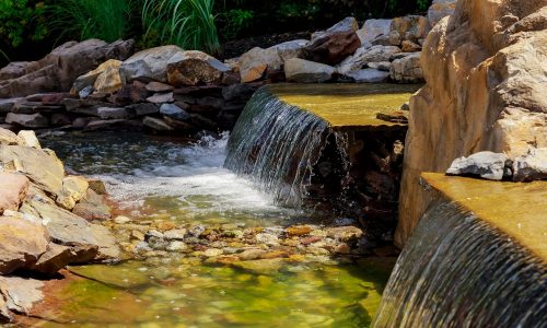 Waterfall at the source. Small Modern fountain in the park on the summer territory. A small fountain in the middle of a small artificial lake